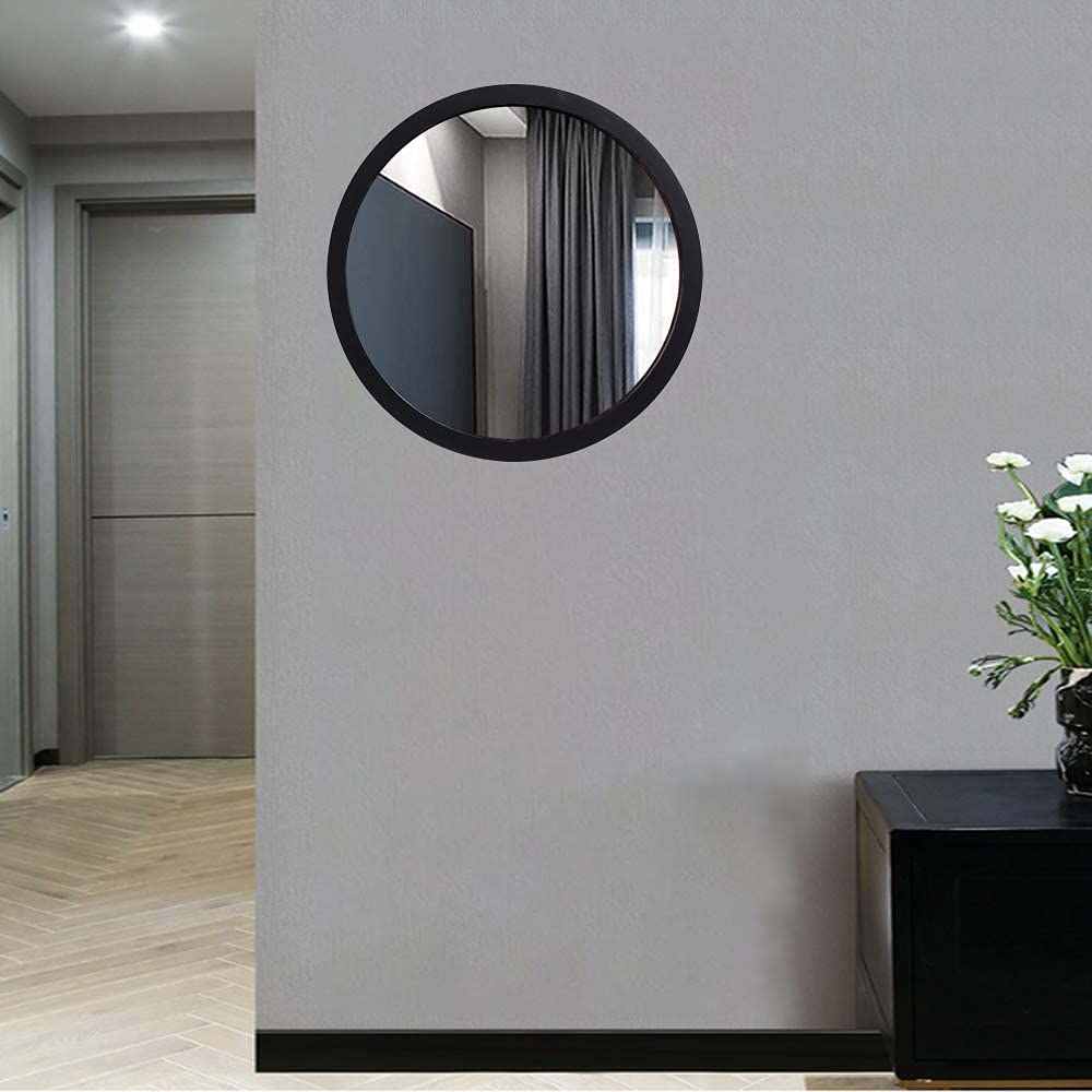 Round mirror on a wall with a vase of flowers on a table in the foreground.