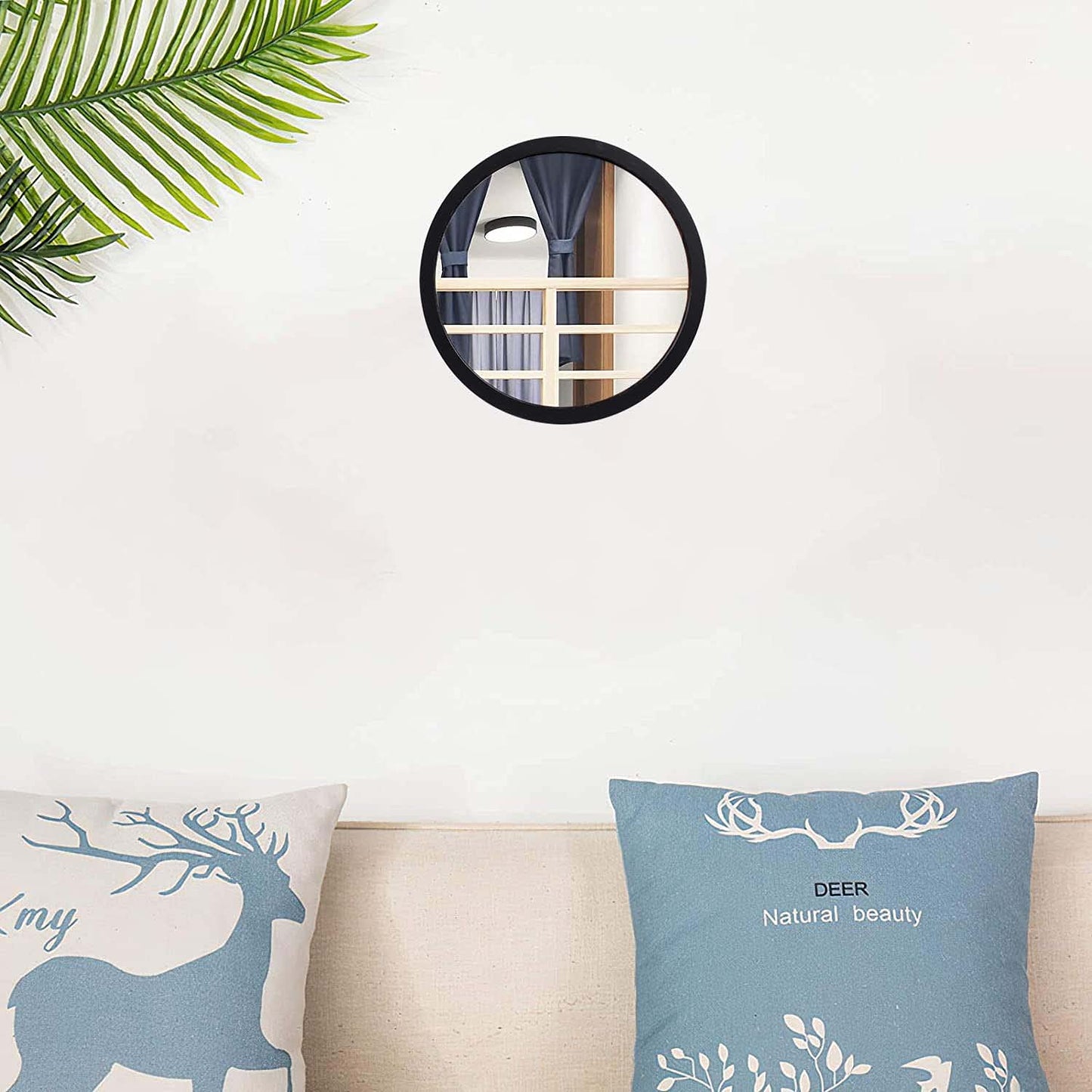 Decorative pillows with deer design on a sofa, mirror above, and plant to the side.